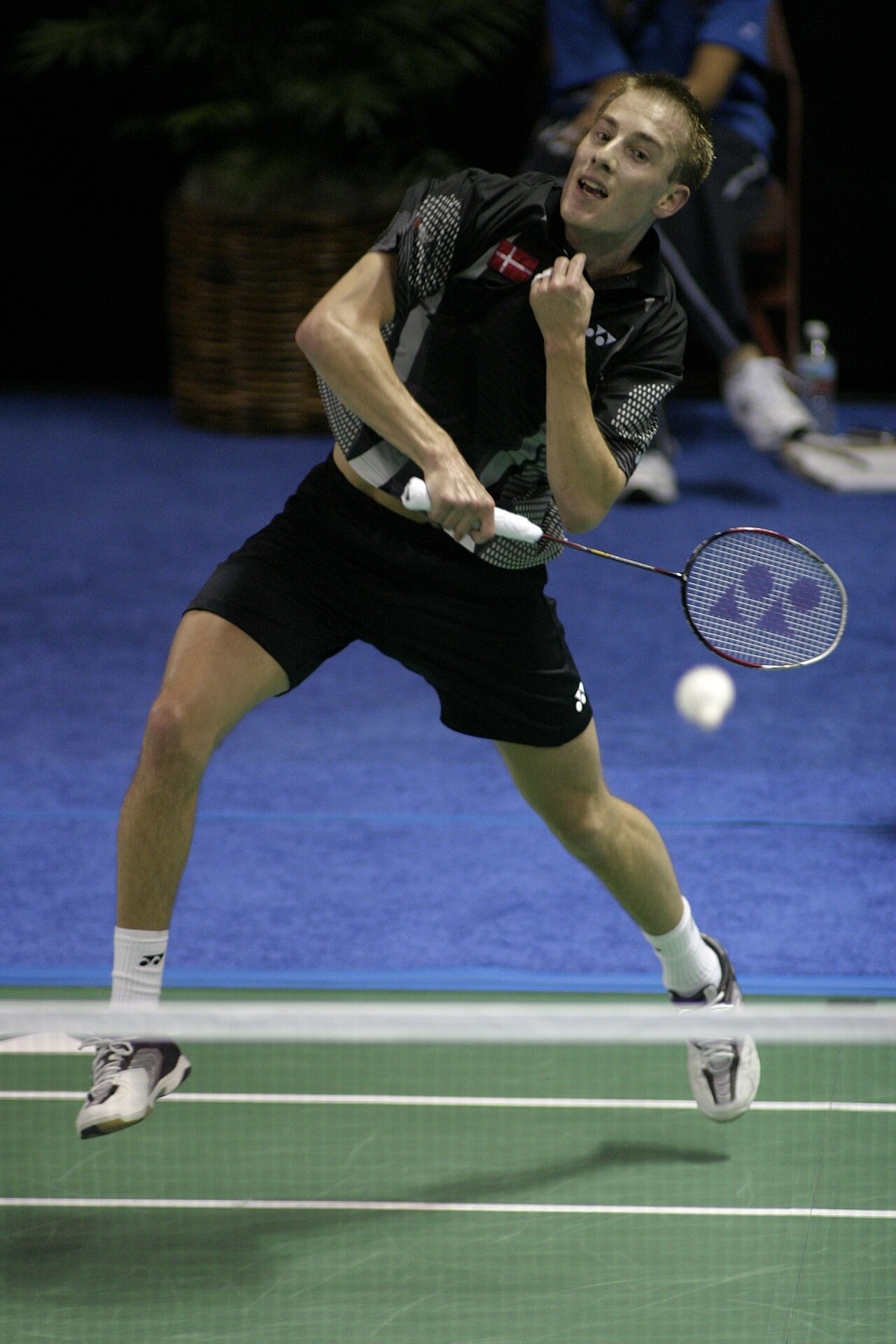 Badminton player Peter Gade airborne at the net, racket swung across his body as he plays a shot just beside the net tape.