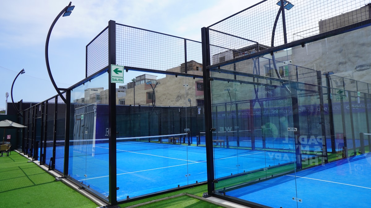 Enclosed padel court with glass back walls and mesh fencing — the distinctive cage layout new players will recognize on day one.