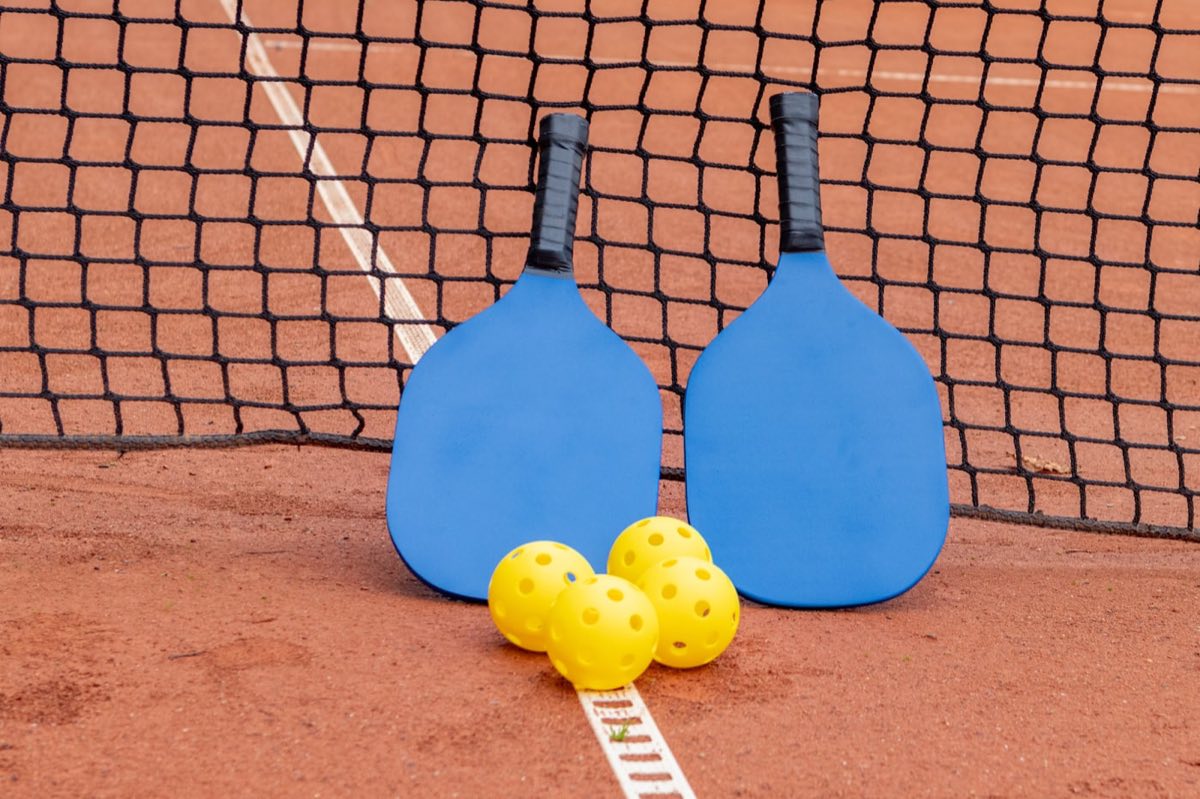 Two pickleball paddles and three balls laid out on a tennis court