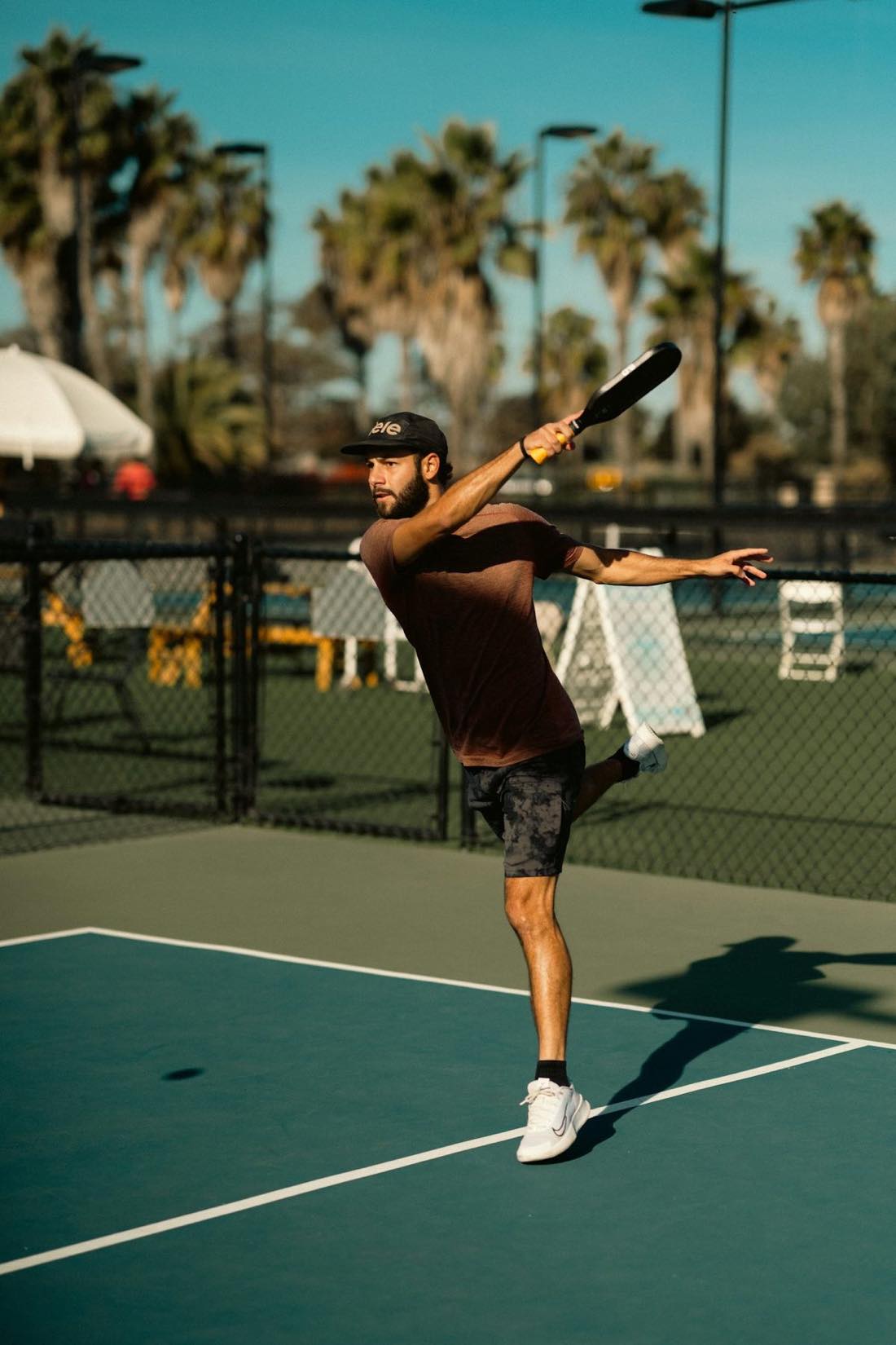 Jugador en solitario golpeando con una pala en una pista de tenis — el tipo de entrenamiento individual que permite una máquina lanzapelotas