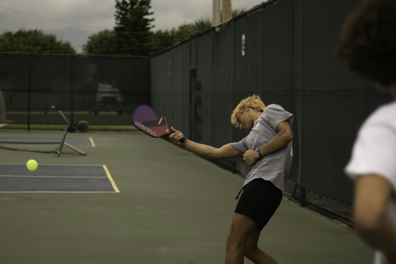 A player swinging a paddle through contact with the ball, generating spin