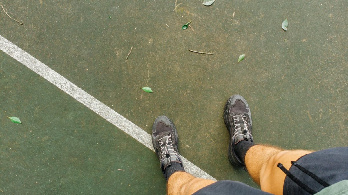 Player's feet planted on a green sport-court surface, mid-stance on the painted boundary line