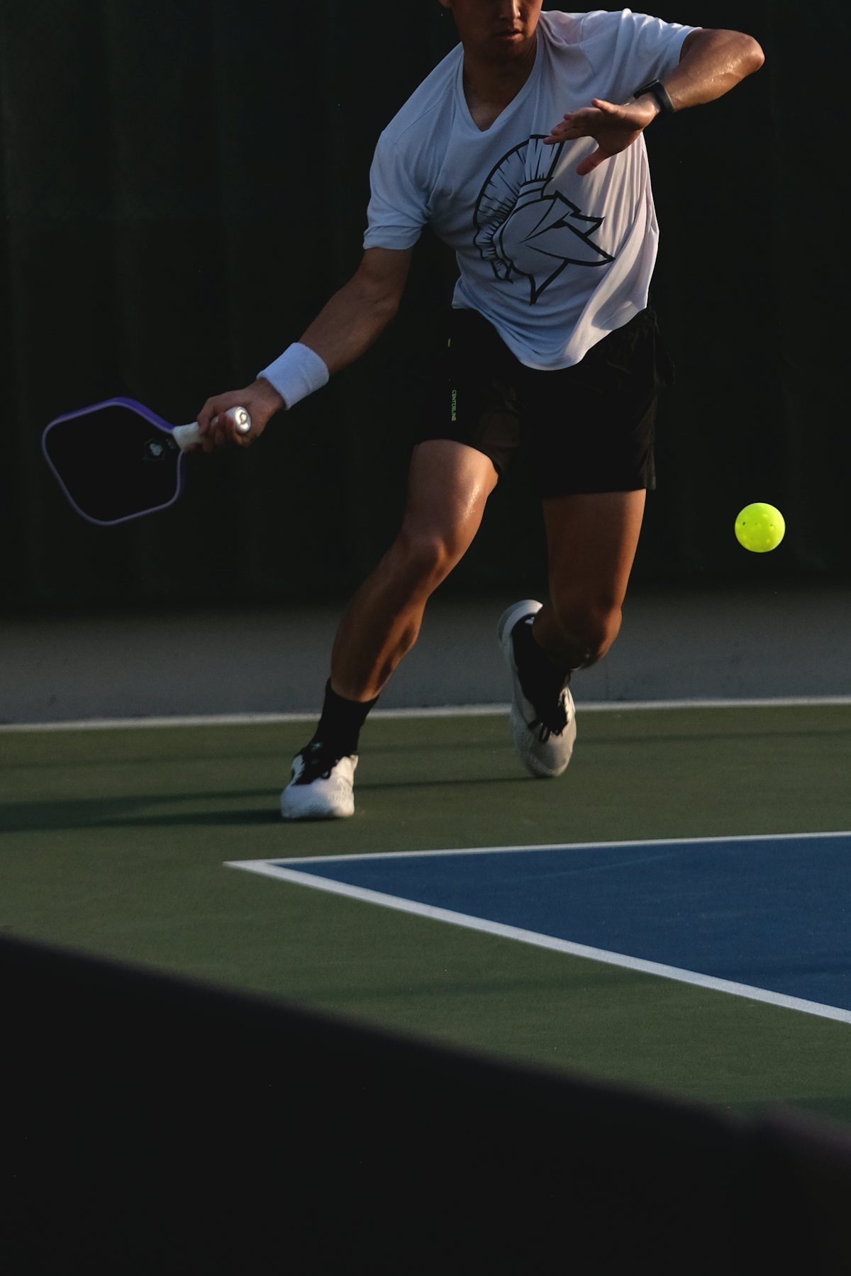 A pickleball player lunging forward with a foot planted right at the non-volley zone line to reach a shot