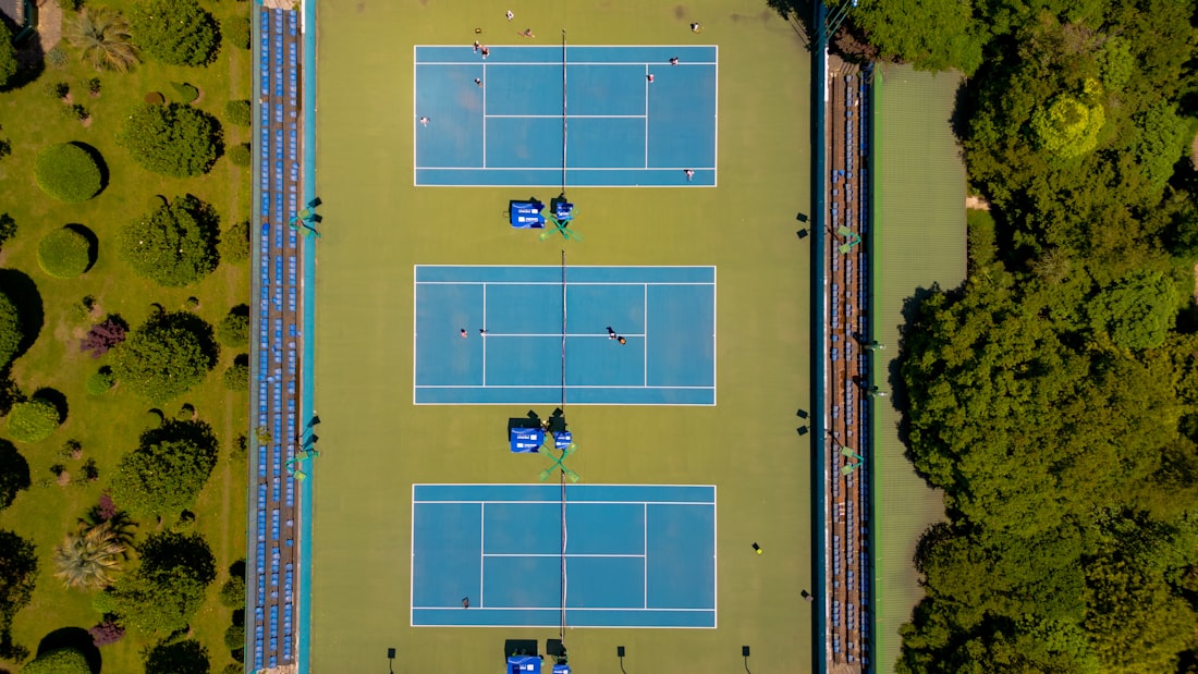 Aerial view of three side-by-side blue and green tennis courts, showing the full court footprint and line markings from above
