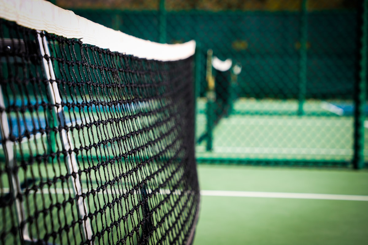 Close-up of a pickleball net's mesh and top tape stretched across a court, with the playing surface visible behind it