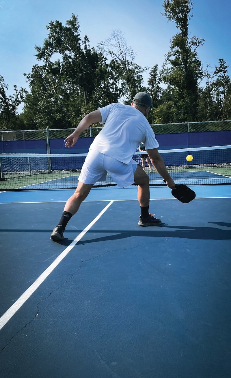 A pickleball player stretching low and wide to reach a ball near the net on an outdoor court