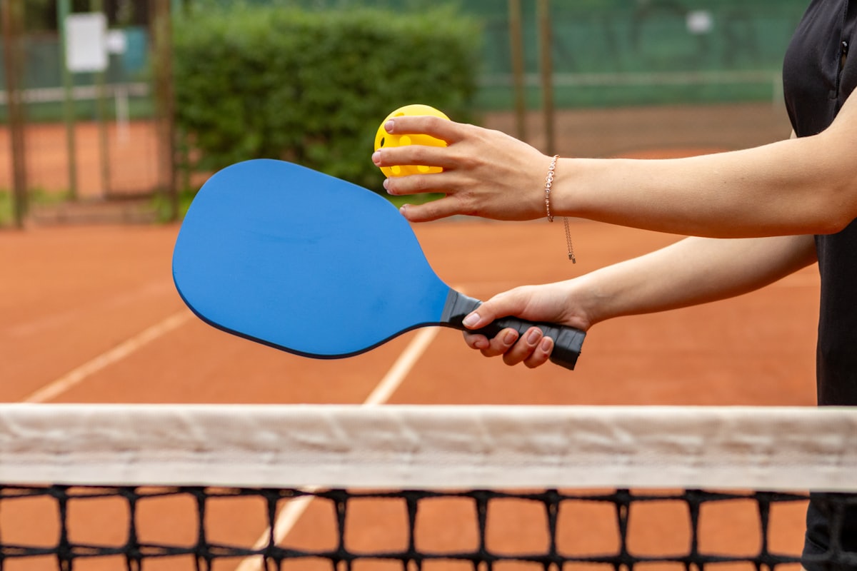 Un jugador sosteniendo una pala y una pelota de pickleball juntas en la red, preparándose para jugar