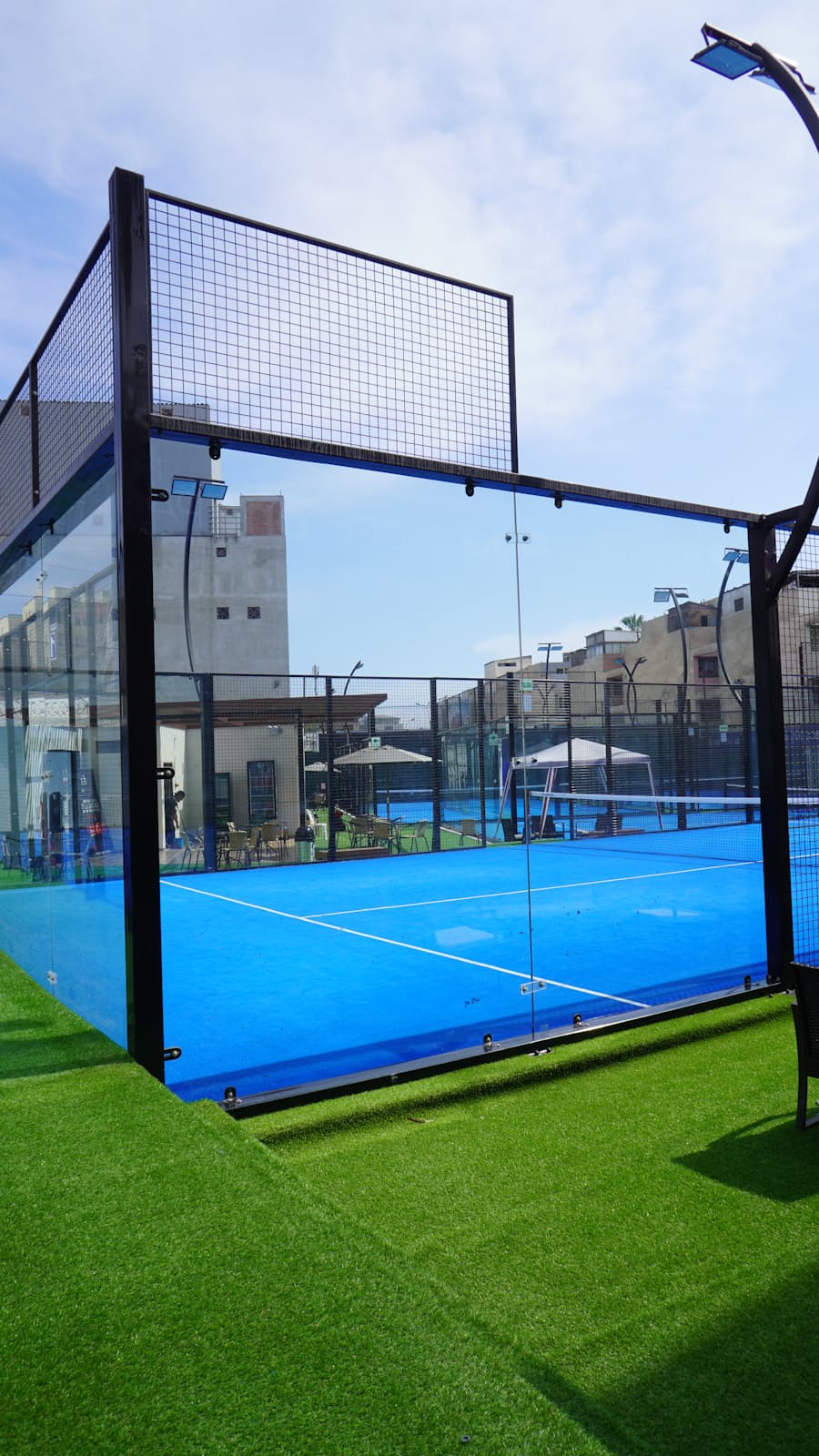 A padel court's net and glass-and-mesh enclosure viewed from the baseline corner, showing the full court layout referenced in the rules tables.