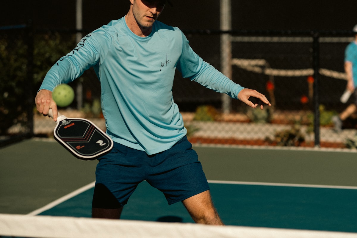 Un jugador de pickleball se inclina bajo cerca de la red para golpear una pelota suave con la pala extendida