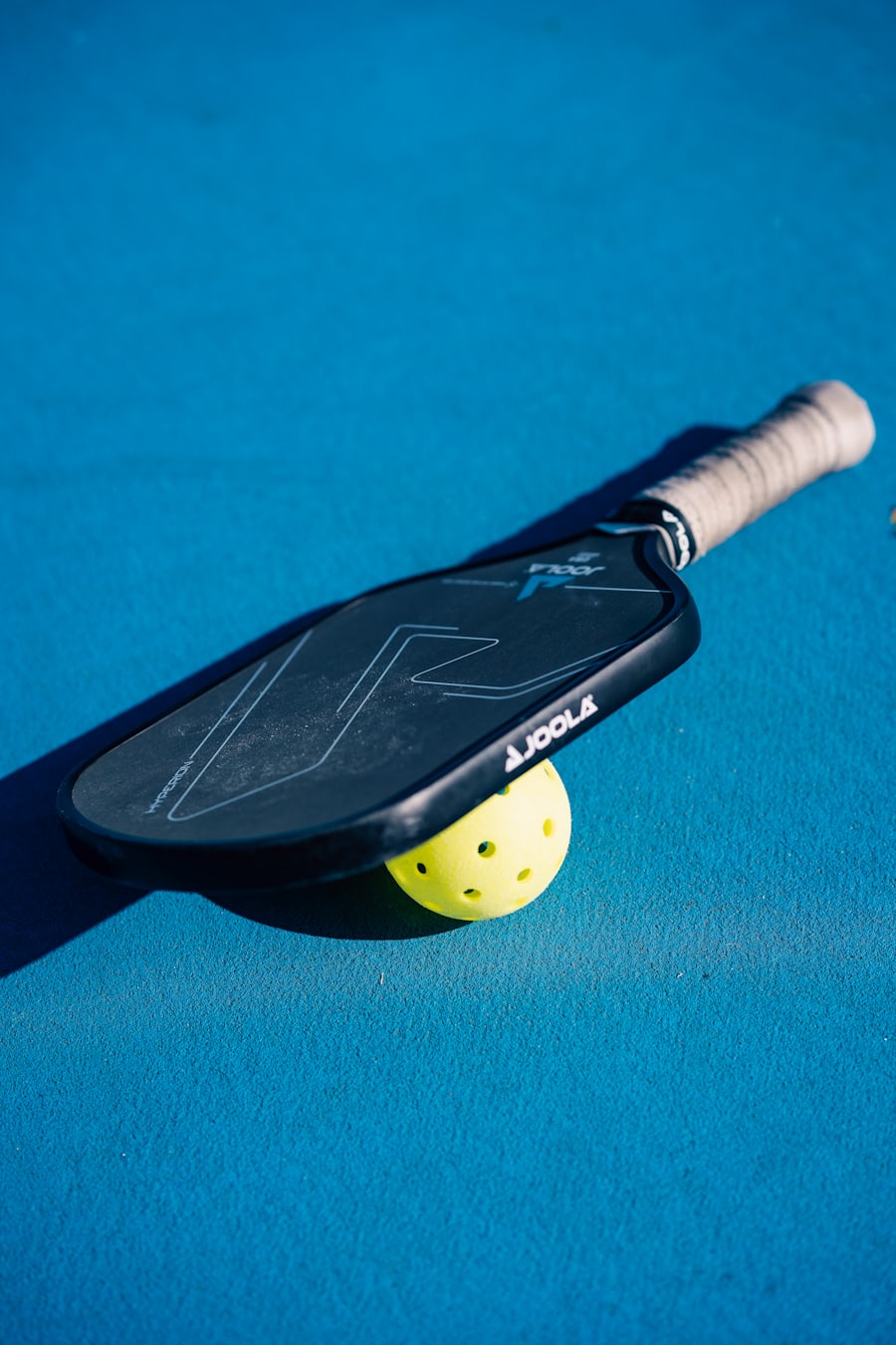 A JOOLA pickleball paddle resting on top of a ball on an outdoor court
