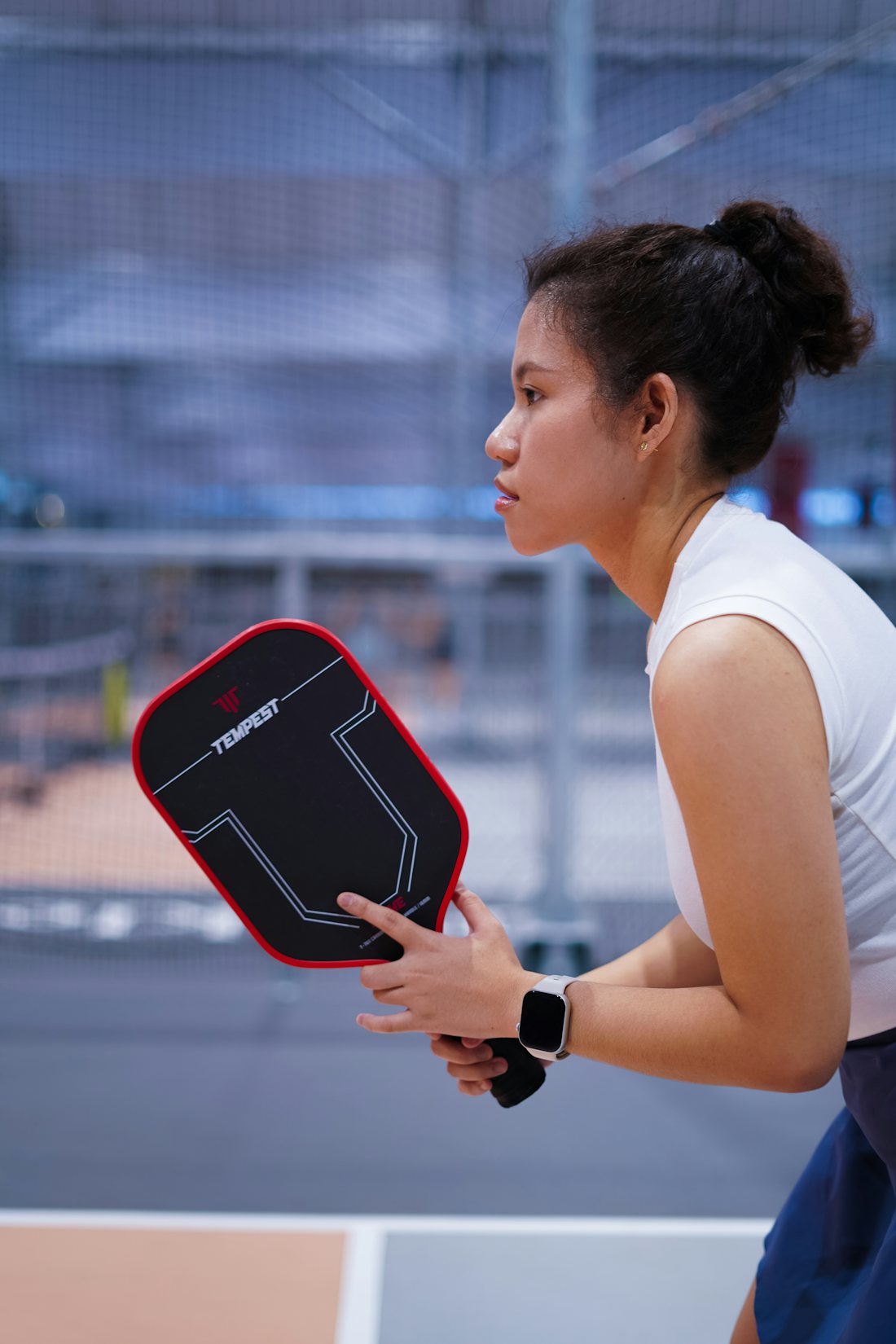 Un jugador sostiene en alto una pala de pickleball negra y roja en posición de espera, con la cara texturizada de material compuesto claramente visible