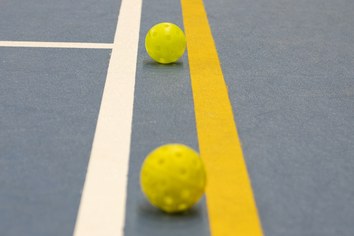 Two pickleballs resting on the white and yellow boundary lines of a court