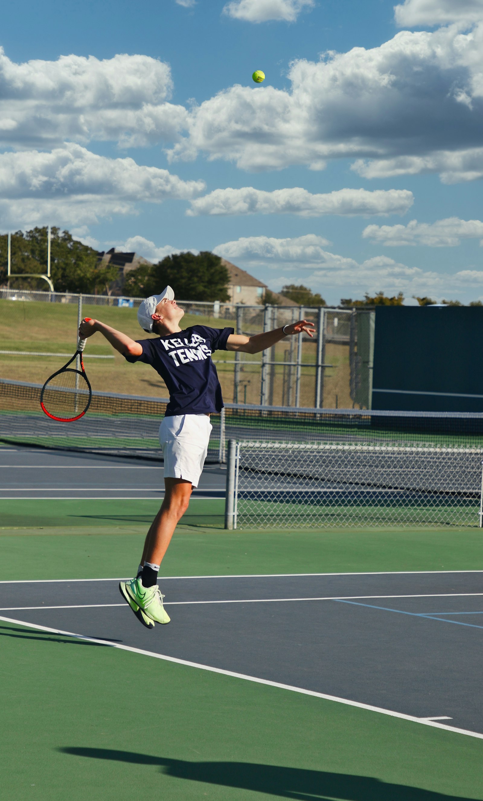 A single tennis player at the baseline, airborne mid-serve with the ball tossed overhead, racket drawn back, no partner or doubles alley in view