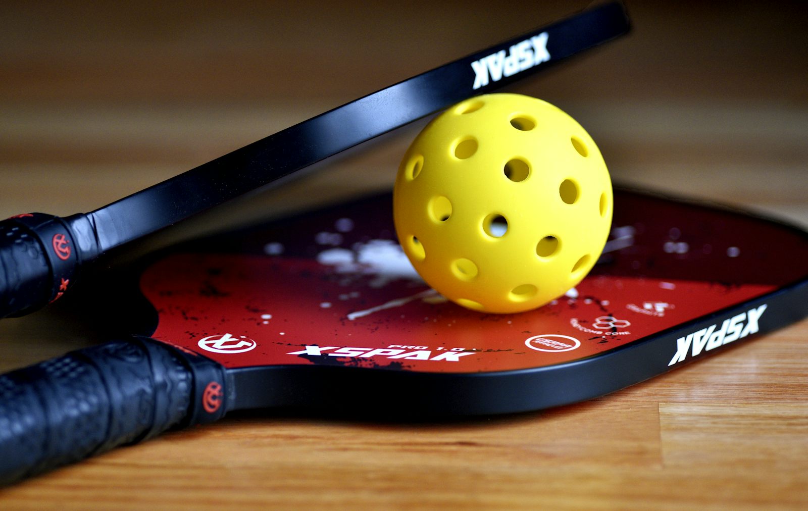 A pickleball resting on a worn paddle face — the surface wear that signals a replacement is overdue