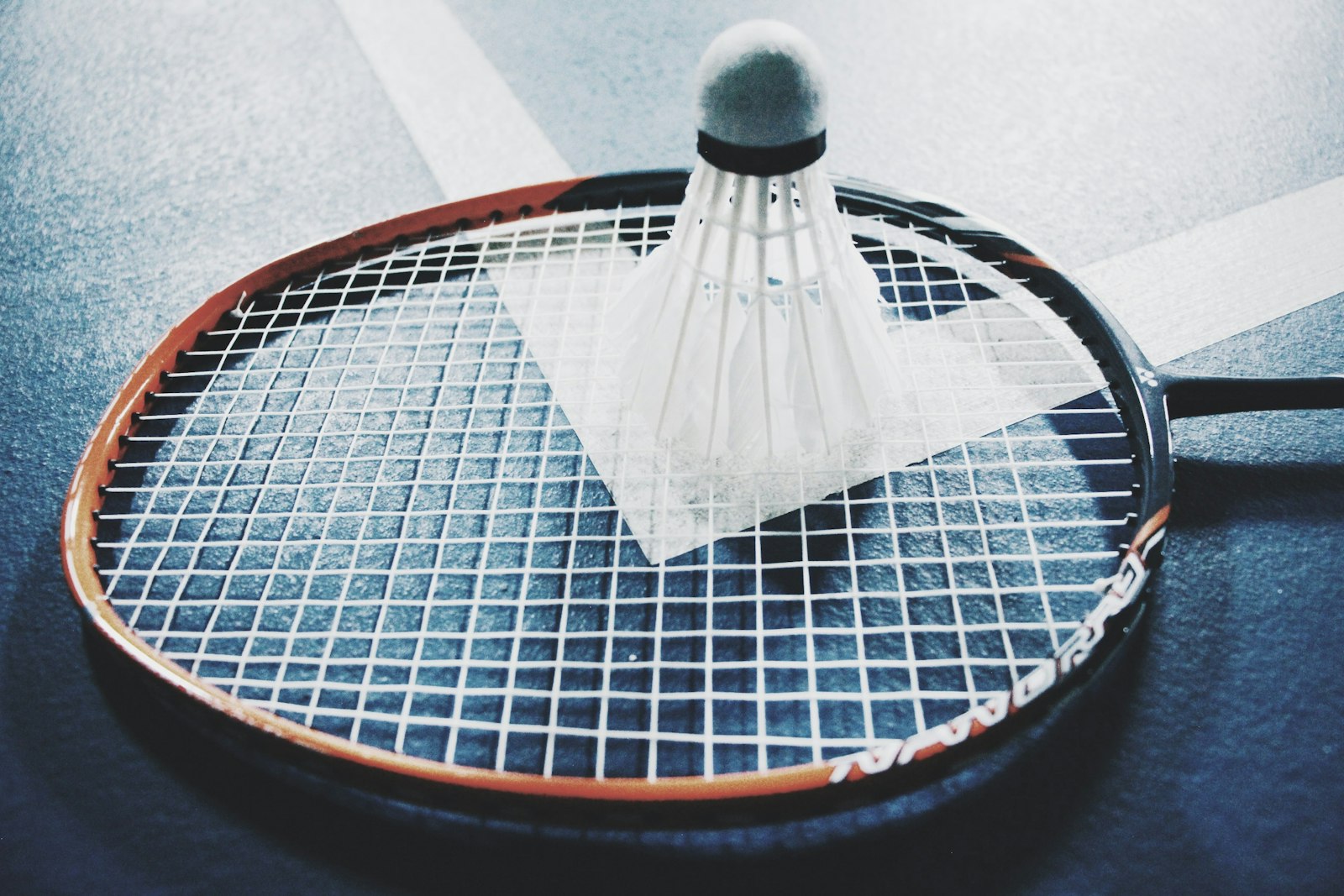 A badminton racket and shuttlecock resting on the white boundary lines of an indoor court