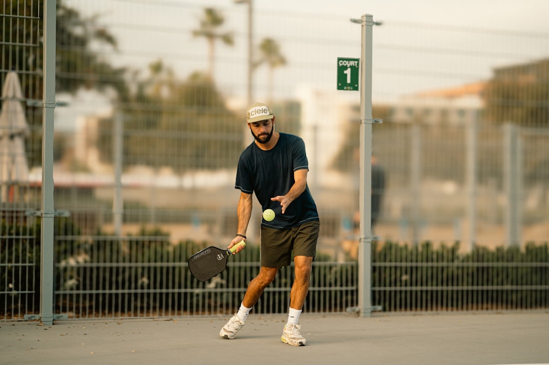 A pickleball player tossing the ball to serve, paddle in hand, at an outdoor community court